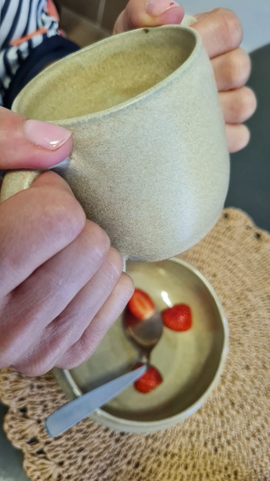 Caneca de dupla alça inclinada sobre o bowl com morangos
