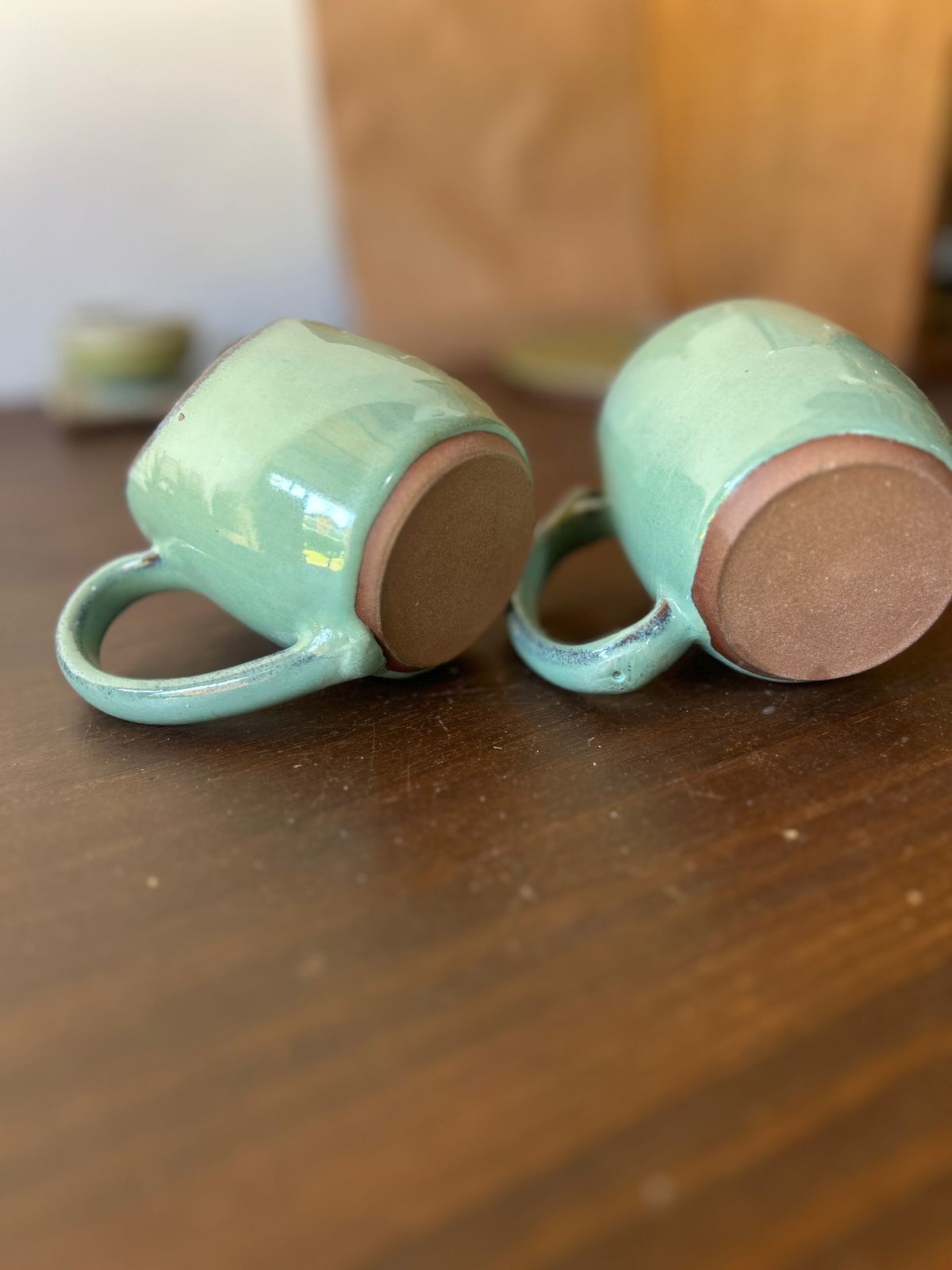 Duas canecas de cerâmica em esmalte verde deitadas sobre a mesa